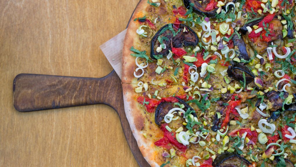 A vegetable pizza on a wooden peel